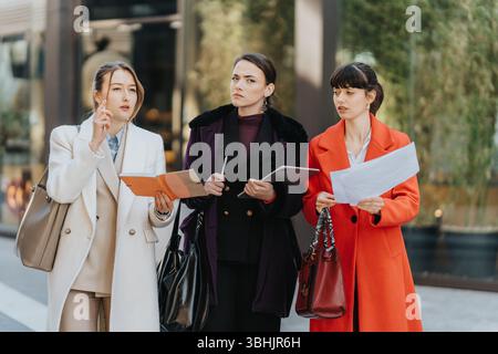 Three female professionals discuss work outdoors holding documents and tablets Stock Photo