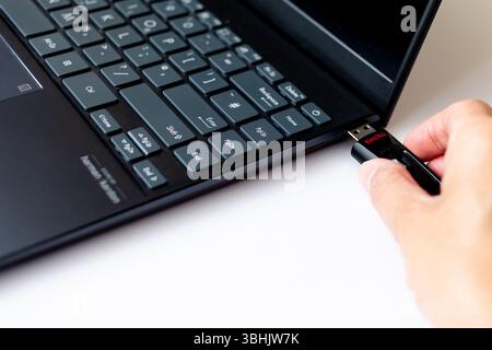 A Sandisk flash drive being placed into a USB port on a laptop Stock Photo