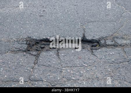 Large pothole on an asphalt road after rain. Cracks in the asphalt pavement. Damaged asphalt highway. Stock Photo