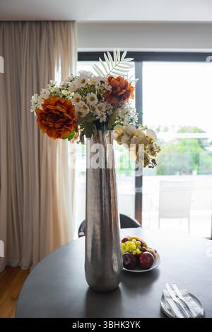 Metallic Vase with Orange and White Flowers on Table by Glass Door Stock Photo