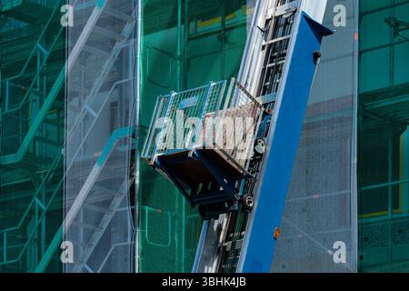 A construction site features a lift used to transport building materials. The lift is positioned alongside a high-rise structure, showcasing green saf Stock Photo