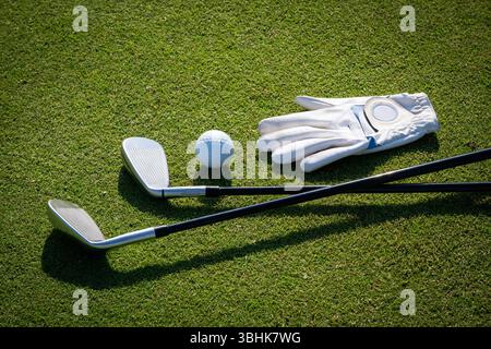 Golf clubs, ball and glove lying on green grass of golf course Stock Photo