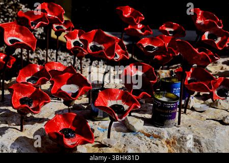 Ceramic poppies surround memorial candles on pale stone at the Car Wall site their red petals & black centers evoking solemn tribute and vivid memory Stock Photo