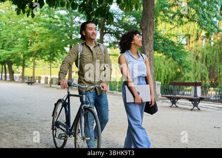Two young colleagues are walking and talking together in a park after leaving work, enjoying the fresh air and discussing their day Stock Photo