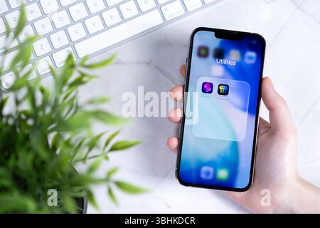 Poznan, Poland - June 10, 2025: Close-up of hand holding a contemporary smartphone, featuring the Utilities folder with apps in the new iOS 26 Liquid Stock Photo