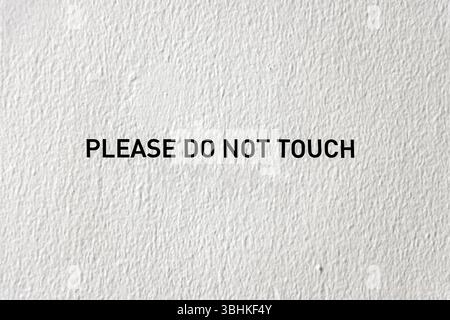 Minimalist black text warning sign indicating 'PLEASE DO NOT TOUCH' displayed on a textured wall surface. Stock Photo