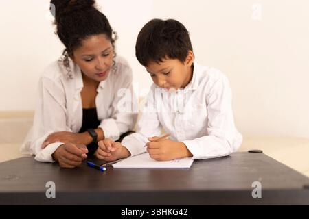 Mother assisting her son with homework at home, focusing on education and homeschooling Stock Photo