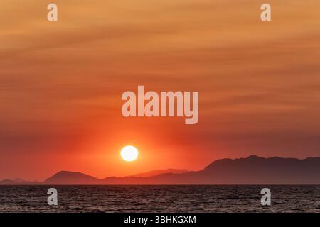 Rhodes Greece. A dramatic setting sun over distant mountains in Turkey and Aegean Sea creates a vivid red sky as the sun nears the horizon Stock Photo