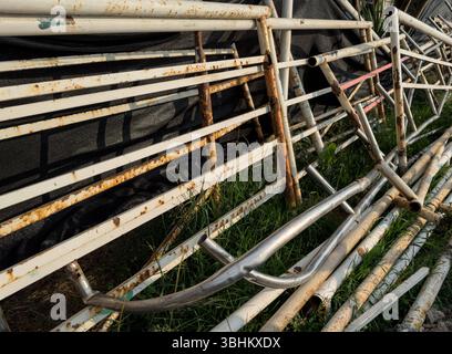 Rusty and bent metal construction frames stacked on grass, shot in daylight with visible texture and industrial mood. Stock Photo