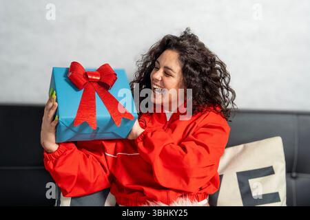 Happy young woman is laughing while holding a blue gift box with a red bow Stock Photo
