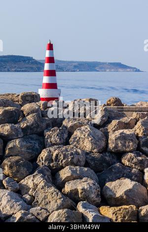 Red and White Striped Lighthouse on Rocky Coastline Near Calm Ocean Waters Stock Photo