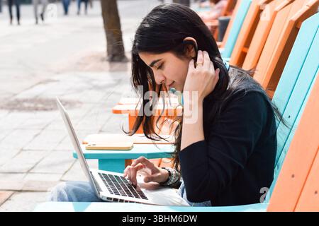 Young woman sitting on city street using laptop computer Stock Photo