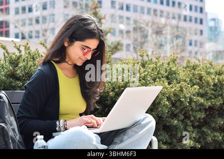 Young happy woman sitting on street bench using laptop computer Stock Photo