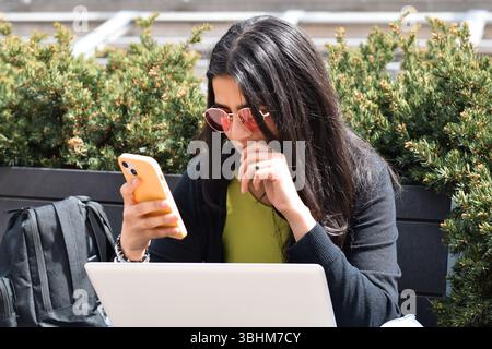 Young woman sitting on street bench using mobile phone Stock Photo
