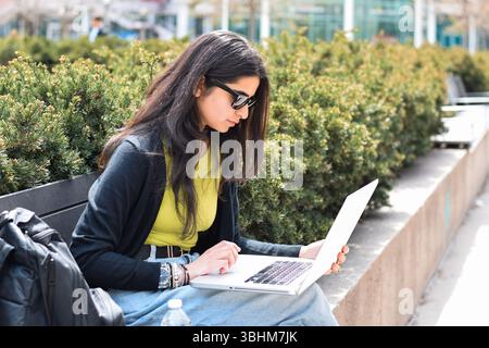Young woman sitting on city street using laptop computer Stock Photo