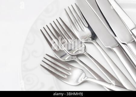 Cutlery set on white plate. Silver fork and knife arrangement. Elegant table setting. Dining utensils for meals. Shiny polished flatware. Stock Photo