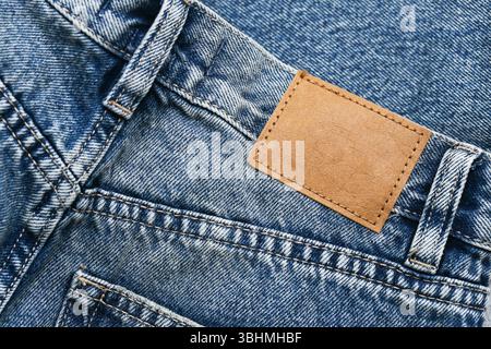 Blue denim jeans with brown leather patch. Back pocket detail. Stylish fashion clothing texture. Urban casual style concept. Close-up of pants fabric. Stock Photo