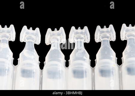 Plastic ampoules in row on black background. Transparent medical packaging. Sterile single-use containers. Concept of hygiene and pharmacy. Stock Photo