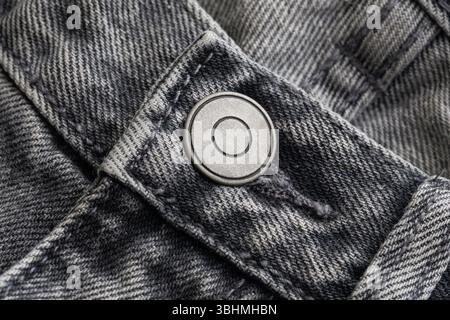 Close-up view of black denim pants. Metal button on jeans. Strong fabric texture. Stylish casual clothing detail. Rough rugged fashion material. Stock Photo