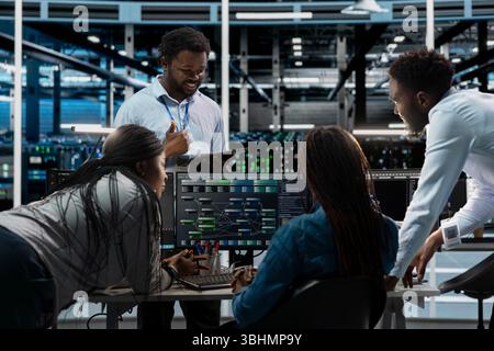 Engineering team programming in AI data center housing advanced equipment used for machine learning training. Server farm workers running code on PC to upgrade artificial intelligence systems Stock Photo