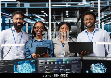 Portrait of happy server farm team looks at data analysis graph to reduce equipment failure. Cheerful data center colleagues look at AI visualization dashboard to pinpoint gear performance glitches Stock Photo