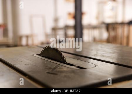 Circular saw blade rising from metal table saw surface in carpentry workshop with warm lighting Stock Photo