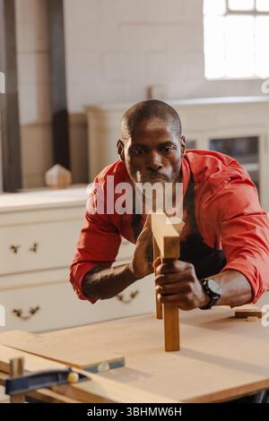 African American man wearing apron using hand plane creating wood shavings on carpentry workbench Stock Photo