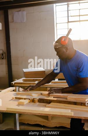 Carpenter using sanding block on wooden plank at workbench inside workshop with sunlight filtering Stock Photo