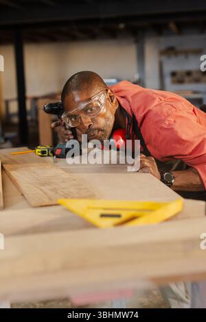 Senior African American man wearing goggles measuring plank at bench using tape measure Stock Photo