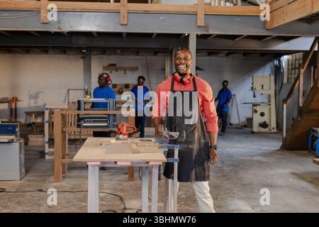 African American male coworkers working on wooden planks in workshop using power sander and clamps Stock Photo