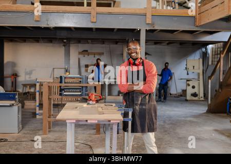 African American male coworkers working at workbench using red electric sander and clamps in shop Stock Photo