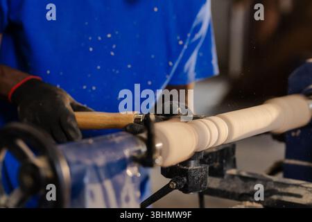 African American man operating wood lathe machine with chisel in workshop, shaping wooden spindle Stock Photo