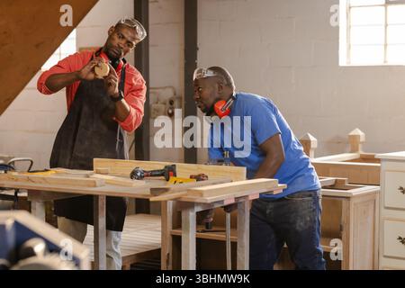 African American male carpenters examining circular cutout at workshop bench with power tools Stock Photo
