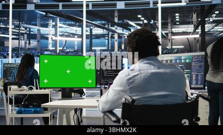 Data center worker with paraplegia using green screen PC to apply node tree programming. Server hub admin with disability uses visual programming on mockup computer to identify data patterns, camera A Stock Photo