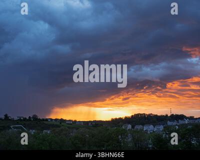 Rain falls from dark storm clouds illuminated by the setting sun over a residential neighborhood outside Pittsburgh, PA. Stock Photo