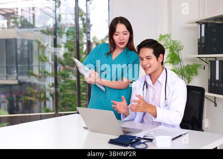 Two young adult Asian medical professionals doctor and nurse collaborating on patient care using a laptop in a bright modern clinic fostering teamwork Stock Photo