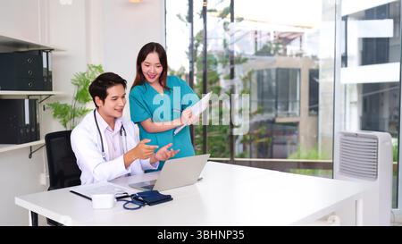 Young Asian doctor and nurse reviewing patient information on a laptop in a modern clinic. Healthcare professionals collaborating on treatment plans. Stock Photo