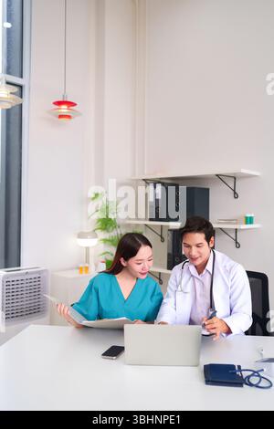 Two Asian healthcare professionals an adult doctor and nurse are collaborating at a hospital desk reviewing documents and a laptop for best patient ca Stock Photo