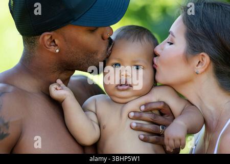 Multiethnic parents and amazed mixed race baby. Multiethnic family outdoor portrait. Happy Multiethnic family hug baby child. Beautiful diverse family Stock Photo