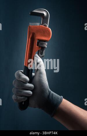 Plumbers hand in glove holding a pipe wrench on blue background Stock Photo