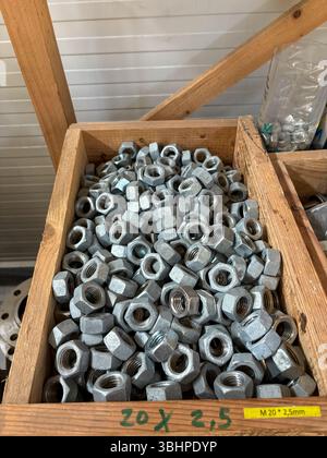 Close-up shot of a wooden crate filled with galvanized metal hex nuts, arranged in an orderly fashion in a workshop. Ideal for illustrating industrial Stock Photo