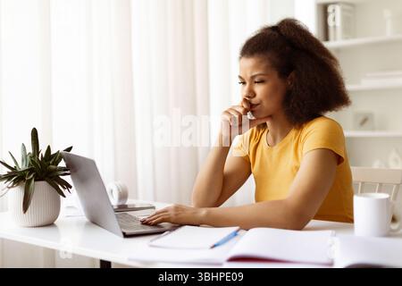 Thoughtful black female working at her desk at home with laptop Stock Photo