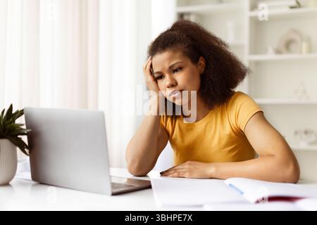 Boring Work. Upset black freelancer woman working on laptop at home office Stock Photo