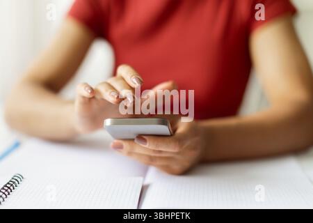 Closeup Shot Of Young Black Woman Sitting At Desk And Using Smartphone Stock Photo