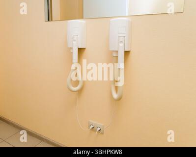 Two electric hair dryers mounted on the wall under the mirror and plugged into electrical outlets. Stock Photo