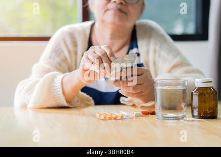 Unhealthy middle aged old woman holding a pill unpacks tablets before use. Old senior people pharmaceutical healthcare treatment concept Stock Photo