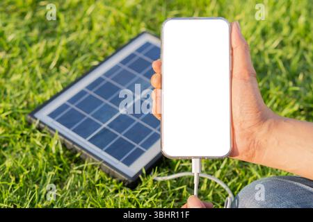 Close-up man's hands holding phone with isolate screen by solar panel on the glass. Charging gadgets with portable solar panel concept. Selective focu Stock Photo
