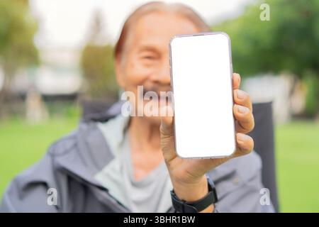 Close up hand of senior man with a beard smiling while standing outside in sunlight, showing mobile phone with blank screen. Copy space. Stock Photo