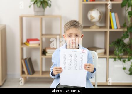 School grade. Sad boy holding answer sheet with letter F indoors Stock Photo