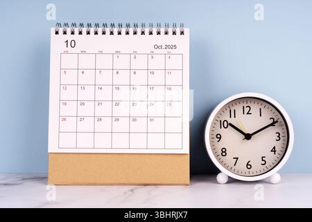 October 2025 desk calendar and analog clock on marble table with blue background, time management concept, work schedule and daily planning Stock Photo